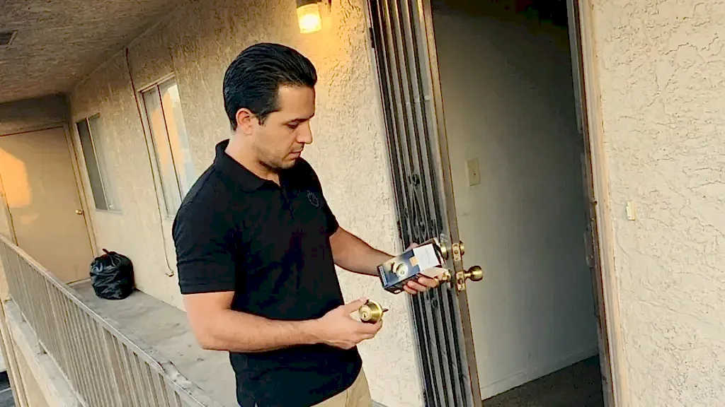 24/7 Locksmith 4U LV technician holding a deadbolt cylinder and a new deadbolt at an apartment door in East Las Vegas