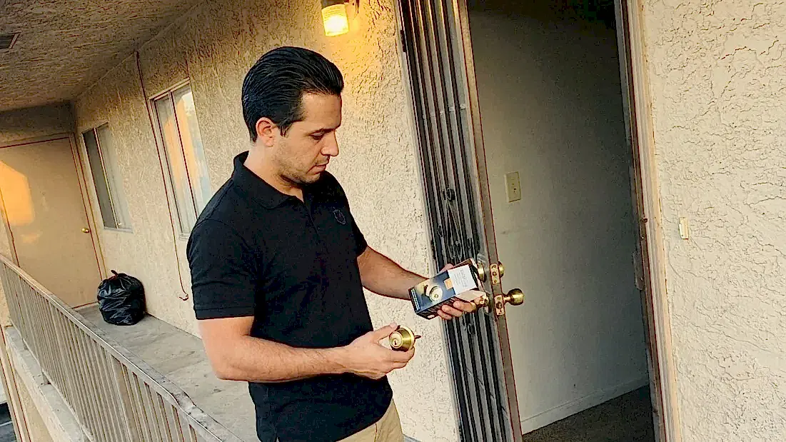 24/7 Locksmith 4U LV technician holding a deadbolt cylinder and a new deadbolt at an apartment door in East Las Vegas